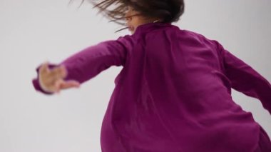 Modern bir dansçı, dinamik, renk değiştiren bir kıyafetle minimalist beyaz bir stüdyoda zarafetle performans sergiliyor.