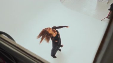 Siyahlı bir kızın, minimalist bir stüdyoda zarafetini ve akıcılığını sergilediği esnek çağdaş dans figürleri sergilediği yüksek açılı bir fotoğraf.