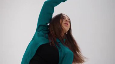 Renk değiştiren bir kıyafetle tek başına dans eden bir dansçı zarif bir şekilde hareket eder. Hareketli kıyafetleri minimalist beyaz bir alanda her adımda yer değiştirir.
