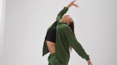 Genç bir kız zarif ve anlamlı bir dans sergiliyor. Temiz, minimalist beyaz bir zemine doğru akıcı bir şekilde hareket ederken kıyafetleri canlı renklerde kayıyor.