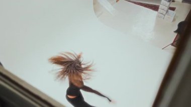 Siyahlı genç bir kızın zarif bir dönüş hareketi ve minimalist stüdyo ortamında akışkan hareketler sergilediği yüksek açılı bir çekim.