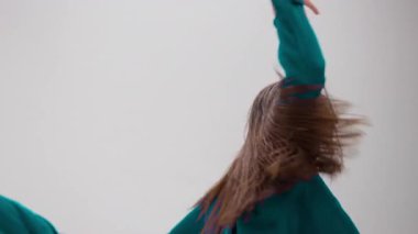 Genç bir kız renk değiştiren bir kıyafetle anlamlı bir şekilde dans ediyor. Hareketleri minimalist beyaz stüdyoyu aydınlatıyor.