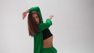 Genç bir bayan dansçı, minimalist beyaz bir stüdyoda hareketini canlı bir görsel yetenekle geliştiren dinamik renk değiştiren bir kostüm giyerek etkileyici ve enerjik bir gösteri sergiliyor.