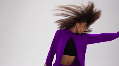 Genç bir kız bir stüdyoda enerjik bir şekilde dans ediyor, her hareketinde değişen dinamik, renk değiştiren kıyafetler sergiliyor.