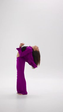Genç bir bayan dansçı dinamik, renk değiştiren bir kıyafetle, minimalist bir stüdyonun temiz arka planına karşı anlamlı bir gösteri sergiliyor.