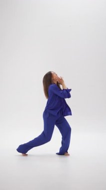 Termokromik giysiler içinde çıplak ayaklı çağdaş bir dansçı minimalist beyaz bir stüdyoda kıyafetleri renk değiştirirken akıcılık ve duygu ile hareket eder.