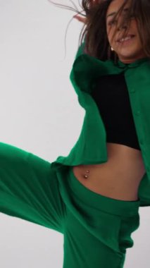 Genç bir dansçı yeşil bir kıyafet içinde zarif bir şekilde hareket eder. Parlak, minimalist bir stüdyo ortamında zarif bir koreografi sergiler.