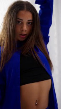 Mavi elbiseli bir kızın minimalist beyaz bir stüdyoda beyaz dantelli perde arkasından zarif bir şekilde hareket ettiği sanatsal solo dans gösterisi.