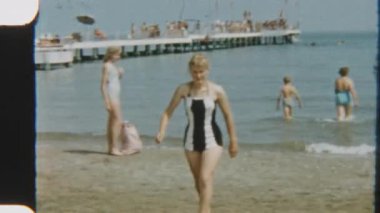 Arka planda hareketli bir iskelesi olan, göl kenarında bikinili bir kadının 8mm 'lik klasik görüntüleri.