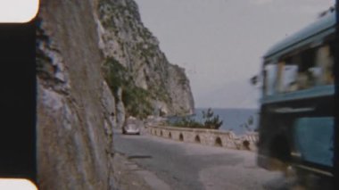 Klasik 8 mm 'lik çekimler klasik arabaları ve kayalık uçurumların oradaki manzaralı bir yolda giden otobüsü yakalıyor. Arka planda Garda Gölü' nün nefes kesici manzarası var.