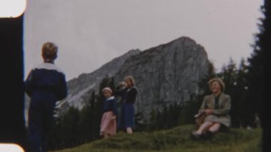 8mm 'lik mutlu bir ailenin arka planda engebeli dağ kayalıkları olan yeşil bir yamaçta dinlenirken doğada bir neşe ve sükunet anı yakaladığı klasik görüntüler.