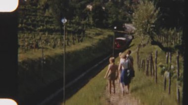 8mm 'lik klasik bir aile görüntüsü, arka planda manzaralı bir köy manzarası olan füniküler bir trenin geçişi sırasında tren raylarının yanında rahatça geziniyor.