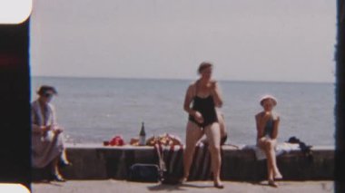 Bir ailenin deniz duvarında rahat bir pikniğin keyfini çıkardığı 8mm 'lik klasik bir görüntü. Manzaralı kayalık bir sahile ve hareketli bir plaja bakıyor.