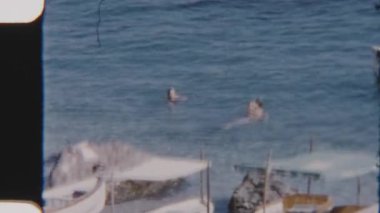 Tatilciler sakin denizde dinlenir ve serinlerler, kıyıya yanaşmış teknelerle.