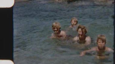 Bir aile sığ deniz sularında yüzmenin keyfini çıkarırken, çarpıcı sahil kayaları resim gibi bir zemin oluşturuyor.