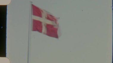 Tahıllı 8 mm 'lik Danimarka bayrağının açık bir gökyüzüne doğru yavaşça dalgalanan görüntüsü nostalji ve ulusal gururu çağrıştırıyor.