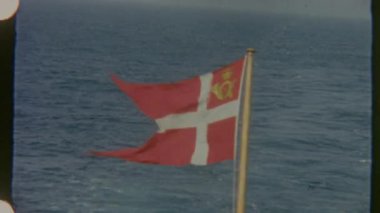 Danimarka 'nın posta bayrağı rüzgarda dalgalanır, engin deniz ufkuna doğru sürüklenir, sakin ama güçlü bir deniz atmosferini yakalar.