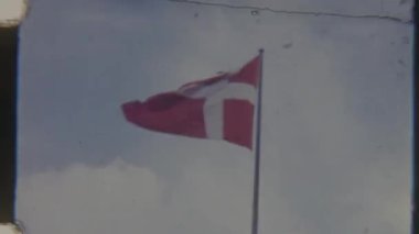 Rüzgarda dalgalanan Danimarka bayrağının, gökyüzüne doğru hareket eden kırmızı ve beyaz bayrağın nostaljik ve klasik bir hissini yakaladığı 8 mm 'lik kumlu görüntüler.