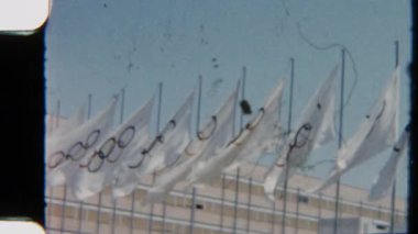 Uluslararası Olimpiyat bayrakları rüzgarda zarif bir şekilde dalgalanıyor, berrak gökyüzüne karşı küresel rekabet ruhunu ve birliği simgeliyor.