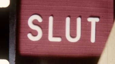 Grainy retro 8mm film featuring the bold Slut title in white text on a striking red backdrop, evoking a vintage cinematic style