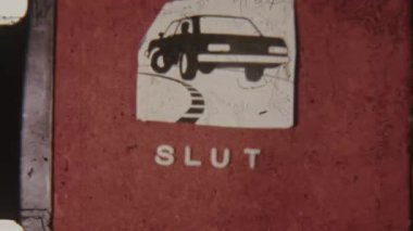 Retro 8mm footage featuring a Slut end title with a car graphic above, set against a bold red background, capturing a vintage, playful aesthetic