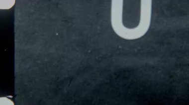 Retro 8mm film efekti, klasik sinematik bir his için klasik buğday ve dokuya sahip siyah bir arkaplan karşısında kalın bir U harfini sergiliyor.