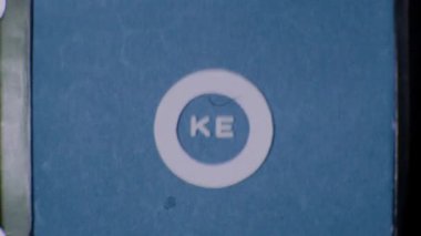 Gri 8 mm 'lik karıncalı görüntülerde KE logosu belirgin bir şekilde mavi bir arkaplanla gösteriliyor. Klasik, eski bir film efekti yakalıyor.