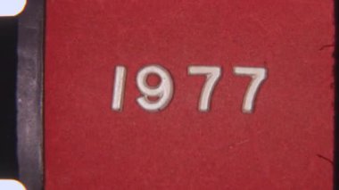 Orijinal 8 mm film dokusuna sahip kırmızı arkaplan üzerine 1977 metni, klasik, kumlu bir görünüm sergiliyor.