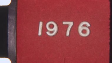 Retro 8 mm 'lik film şeridi, 1976' yı sıkıntılı bir kırmızı arka planda gösteriyor, film tahılları ve dokusuyla klasik bir görünüm sunuyor.