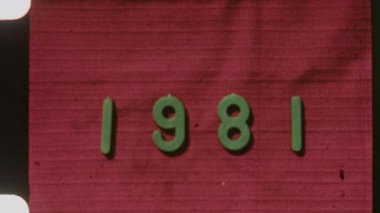 8 mm 'lik film şeridi, 1981 tarihini kırmızı desenli bir arka planda sergiliyor. Eski, kasvetli bir film dokusuyla nostaljik bir his yakalıyor.