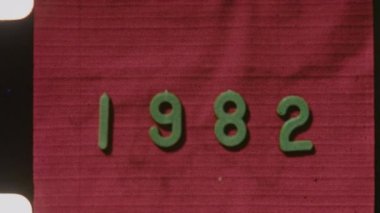 Grainy 8mm film lideri 1982 'yi kırmızı desenli arka planda otantik bir görünüm için görünür çizikler, titreme ve çıkıntı delikleriyle gösteriyor.