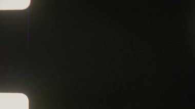 Siyah bir arkaplan üzerine kurulmuş 8 mm 'lik bir film, özgün film çıkıntısı deliklerini taklit etmek için sol üstte ve altta iki parlak, yuvarlak dikdörtgen ışık noktası içerir.