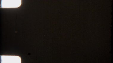 Bu koyu 8mm 'lik film örtüsü ince tanecikler ve hafif çizikler ile güçlendirilmiş simsiyah bir zemin içerir, görünür çıkıntı delikleri nostaljik bir dokunuş ekler.