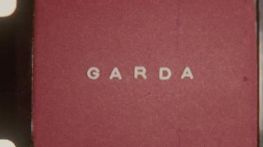 8 mm 'lik bir film klipinde GARDA kelimesi koyu kırmızı-kahverengi bir arka planda hafif beyaz harflerle gösterilir, ince bir dokusu ve küçük kusurları vardır.