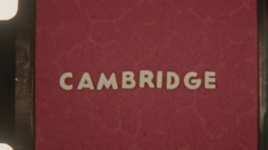 Cambridge sözcüğünün koyu, beyaz retro-stil harf içerdiği 8 mm 'lik klasik bir film çerçevesinin yakın çekimi, dokulu kırmızı arka plan üzerine kuruludur.