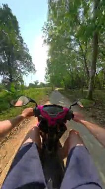 Ormanın derinliklerinde, yoğun yeşillik ve doğal ortam ile çevrili dar bir toprak yolda motosiklet sürüşü.