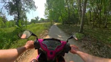 Dar bir yolda pürüzsüz süzülen sakin bir scooter sürüşü, canlı yeşil ağaçlar ve yoğun orman yapraklarıyla çevrili, doğanın barışçıl özünü yakalıyor.