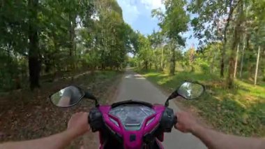 POV scooter sürüşü verimli bir tropikal orman yolu boyunca süzülürken berrak mavi gökyüzünün altında ağaçların arasından süzülen güneş ışığı ve özgürlük ve macera hissi ile birlikte.