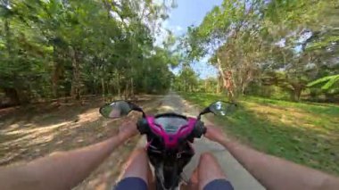 Yoğun yeşilliklerle çevrili dar bir orman yolunda scooter süren bir adamın görüntüsü doğa ve hareketin barışçıl ve sürükleyici deneyimini yakalıyor.