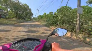 Ağaçlarla çevrili sakin kırsal bir arazide scooter gezintisi, huzurlu bir atmosfer, hafif bir esinti ve doğal yeşillik sakin ve manzaralı bir yolculuk yaratıyor.