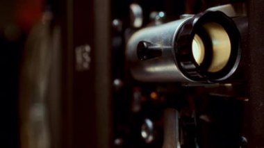 Dönen bir film makarasını ve parıldayan lensi aksiyon halinde gösteren klasik bir film projektörünün yakın çekimi