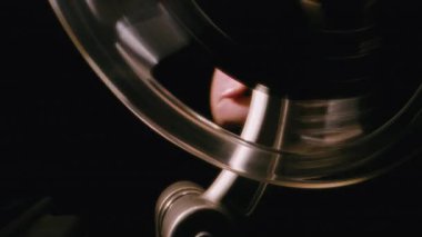 Eski bir film projektörünü elle çalıştırmak için filmin makarasını sürekli hareket halinde çevirerek klasik film projeksiyonunu iş başında göstererek yakın plan çekiyoruz.