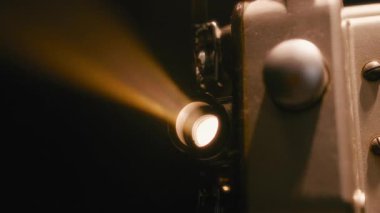 Karanlık bir odada parlayan ve ışık saçan klasik bir film projektörü merceğine yakın plan projeksiyon sırasında klasik bir sinema atmosferi yaratır.