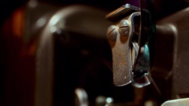 Antik bir film projektörünün yakın çekimi, film şeridini roket montajında sorunsuzca hareket ederken gösteriyor, klasik mekanik detayları vurguluyor.