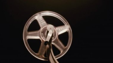 8mm 'lik bir film şeridine yakın çekim. Krank kolu filmi ilerletmek için döndükçe vintage bir projektörün makarasına bağlanıyor.