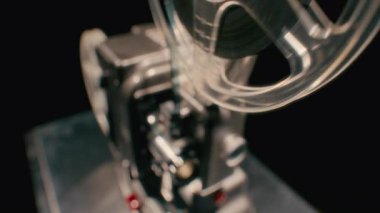 Klasik bir analog film projektörü güç verir, makarasını döndürür ve yavaş yavaş kapanmadan önce film şeridini sorunsuzca hareket ettirir.