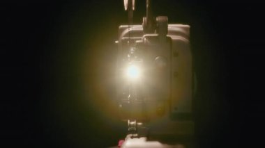 Klasik film projeksiyonunun nostaljik sihrini yakalayan, eski bir film projektörünün objektifinden parlayan parlak bir sinema ışığına zum yapıyorum.