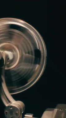 Eski moda film projeksiyonunun nostaljik mekaniğini yakalayan klasik bir film projektörünün makarasını elle döndüren bir eli gösteren detaylı bir yakın çekim.