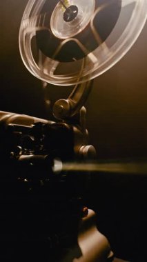 Yavaş dönen bir film makarası olan klasik bir klasik film projektörü lensten parlak bir ışık huzmesi yansıtıyor ve nostaljik bir sinematik atmosfer yaratıyor.