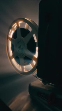 Klasik bir film makarası, eski moda sinemanın nostaljik çekiciliğini yakalayan, sıcak ışıkla hafifçe aydınlatılan klasik bir projektör üzerinde yavaşça dönüyor.